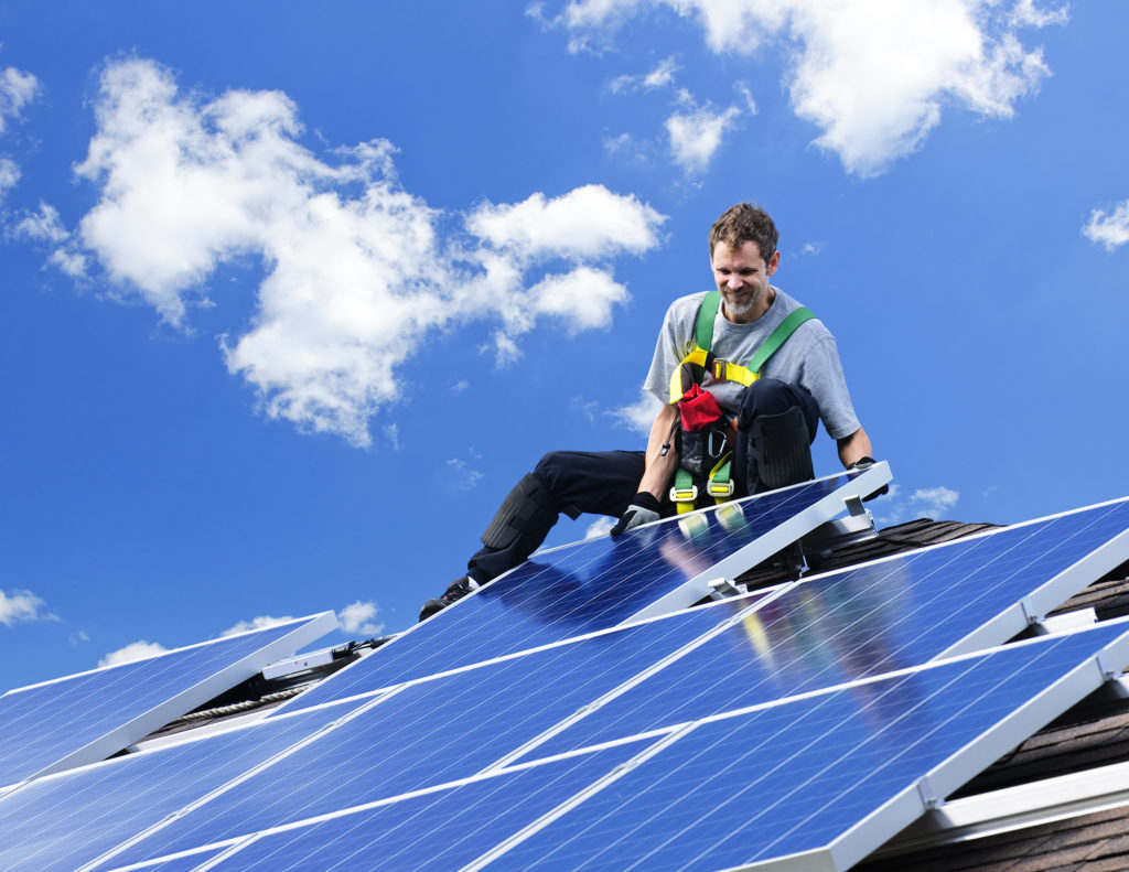 Worker installing alternative energy photovoltaic solar panels on roof